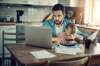 Psychologie Student sitzt mit Kind auf dem Schoß vor Laptop am Küchentisch