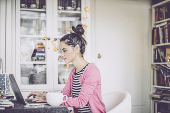 Eine Fernstudentin für Gesundheitspsychologie sitzt zu Hause am Laptop und lernt für das Fernstudium