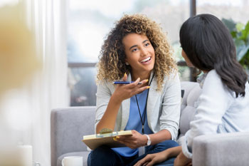 Eine Gesundheitspsychologin sitzt mit einer Patientin zum Gespräch auf einem Sofa