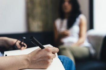 Ein Klinischer Psychologie ist mit einer Klientin im Gespräch, die ihm gegenüber auf einem Sofa sitzt.