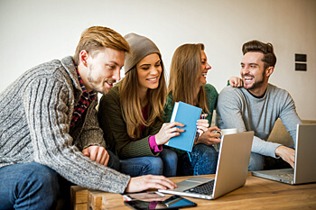 Vier Psychologie Studenten lernen und lachen gemeinsam an einem Holztisch mit Laptops