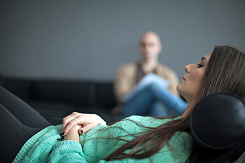 junge Frau auf Sofa mit Mann im Hintergrund