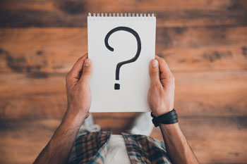 Student hält ein Fragezeichen auf einem Block in der Hand