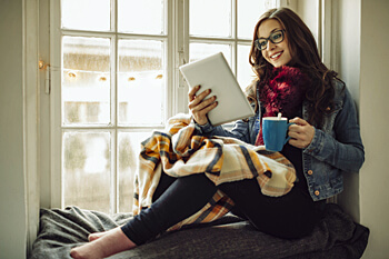 Psychologie Studentin sitzt auf Fensterbank mit Kaffeetasse und Tablet in der Hand