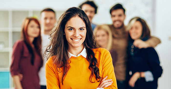 Psychologie Studentin lächelt in die Kamera, im Hintergrund sind weitere Psychologie Studenten