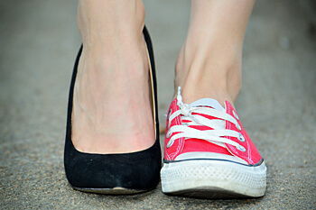 Nahaufnahme von den Füßen einer Frau mit einem Fuß in hohen Schuhen und einem in Sneakers